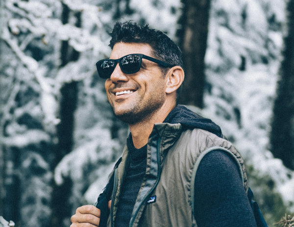 A man stands outside in a snowy forest wearing flexible, polarized and magnetic MagLock Sunglasses by Distil Union